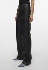 Zwarte leren wide-leg broek met hoge taille, gladde textuur en klassiek vijf-pockets ontwerp, gecombineerd met lichtblauwe puntige schoenen.