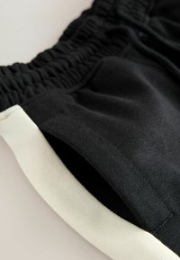 Black shorts with an elastic waistband and cream-colored trim. Features a soft, textured fabric and a side pocket opening.