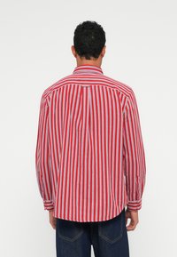 Rød og hvit stripete skjorte med lange ermer, knappelukking på kragen og rund kant, med standard mansjetter og bakstykke detaljer.
