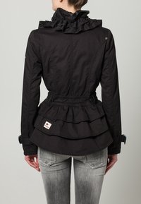 Svart jacka med rynkad krage, flerstegs peplumdesign, justerbar midja och en logotypmärke på nedre ryggen. Texturerat tyg, figursydd stil.