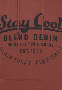 Felpa bordeaux con grafica frontale. Il testo recita "Rimani fresco, mescola il denim", "Di cosa sei ricco?" e "Rivendica i tuoi diritti sul denim". Aglet dorati.