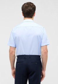 Korte mouwen lichtblauw shirt van gladde stof, voorzien van een button-down kraag. Gecombineerd met donkerblauwe op maat gemaakte broeken.