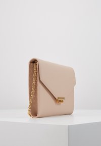 Béžová kabelka z umělé kůže s řetízkovým popruhem, trojúhelníkovým klopou a zlatou sponou s logem. Hladká textura, minimalistický design.