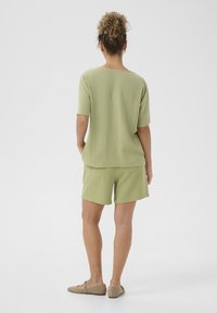 Lichtgroen kort mouwtopje en bijpassende shorts, gemaakt van een gestructureerde stof. De outfit heeft een losse pasvorm en wordt gecombineerd met beige instappers.