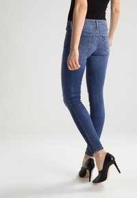 Vaqueros ajustados azul oscuro con una textura de mezclilla suave, que cuentan con bolsillos traseros y una etiqueta de marca discreta. Combinados con zapatos de tacón alto negros.