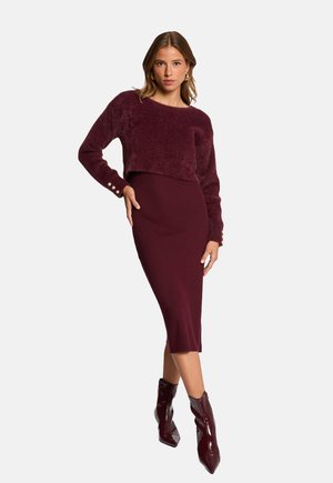 Maglione corto bordeaux in morbido tessuto abbinato a un vestito a coste lungo fino al ginocchio, accentuato da stivaletti lucidi con punta.