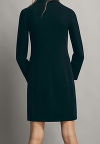 Figurbetontes, langärmeliges Kleid aus dunkelgrünem Stoff. Das Design verfügt über einen hohen Kragen und zwei seitliche Taschen, mit einer glatten Textur.