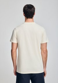 Koszulka z krótkim rękawem, okrągłym dekoltem w jasnym beżowym kolorze z bawełny. Gładka faktura, luźny krój, prosta konstrukcja z tradycyjnym prostym dołem.