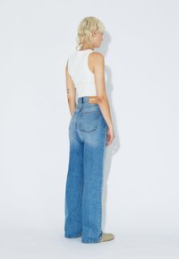 High-waisted light blue denim jeans with a relaxed fit, featuring a leather patch on the back and labelling on the waistband.