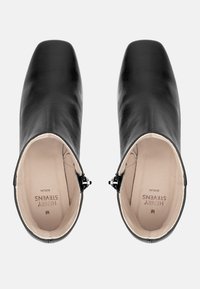 Bottines en cuir noir avec une finition lisse, bout carré et fermeture éclair. Intérieur doublé de beige avec un branding subtil.