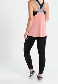 Rosa atletisk tanktop med grå detaljer, parret med sorte leggings med netdetaljer. Fodtøjet har en lys grå og mørk pink farveskala.