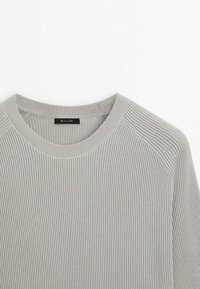 Pull à côtes gris clair avec un col rond et des manches raglan. Le tissu a une finition texturée et présente une étiquette de marque au niveau du cou.