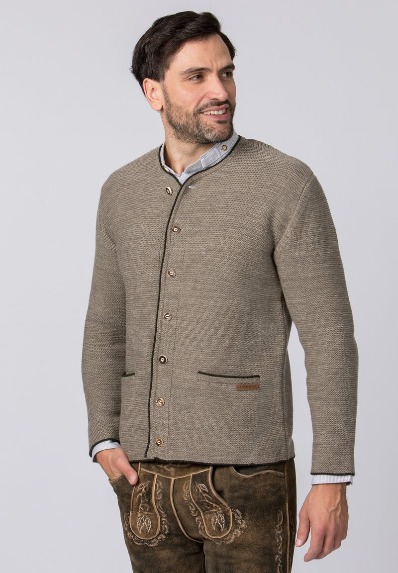 Hellbrauner Strickcardigan mit rundem Kragen, braunen Knöpfen und zwei vorderen Taschen. Akzentuiert mit dunklen Abschlüssen und einem Markenetikett.