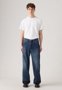 Witte katoenen t-shirt, comfortabele pasvorm, gecombineerd met blauwe wijde jeans met een klassieke vijf-pocket ontwerp en subtiele vervaging. Zwarte schoenen.