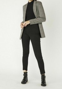 Šedý kostkovaný blejzr přes černý žebrovaný rolák, doplněný černými skinny jeans a černými šněrovacími kotníkovými botami. Hladká textura, perfektní střih.