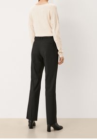 Hellsrosa langärmliger Pullover kombiniert mit schwarzen, taillierten Hosen, die über zwei Gesäßtaschen verfügen, und abgerundet mit schwarzen, hohen Ankle Boots.