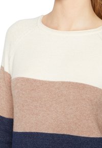 Pull en maille avec rayures horizontales crème, beige et bleu marine. Texture douce avec un col rond et des manches raglan.
