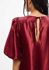 Μπορντό σατέν τοπ με φουσκωτά μανίκια, που διαθέτει άνοιγμα στην πλάτη δέσιμο με λεπτή λωρίδα και απλή υφή.