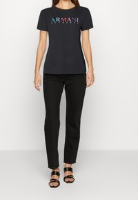 Černé bavlněné tričko s barevným logem "ARMANI EXCHANGE", krátkými rukávy a kulatým výstřihem, v kombinaci s černými úzkými džíny a sandály na řemínky.