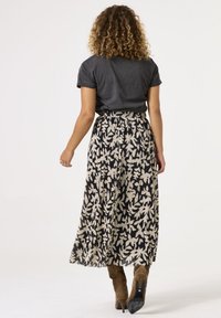 Maxikleid aus einem floral gemusterten, plissierten Stoff in Schwarz und Creme, kombiniert mit einem taillierten grauen T-Shirt und braunen High Heels.