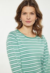 Top cu mâneci lungi în dungi verzi și albe, cu guler rotund. Textură fină, design ajustat și detalii subtile de-a lungul gulerului.