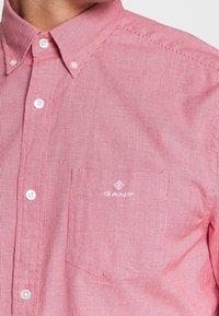 Rood-wit gestreept overhemd met knopen, van katoenen stof, met een borstzak en bedrijfslogo in wit. Heeft een klassieke kraag en knopen.