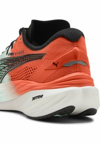 Zapatilla de running Puma con parte superior de malla roja y negra transpirable, una entresuela blanca en contraste y un destacado logo "NITRO" en la suela.