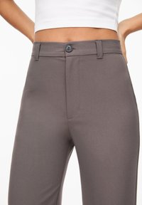 Pantalons gris ajustés en tissu lisse, dotés d'une fermeture à bouton à l'avant, de passants de ceinture et de deux poches latérales.