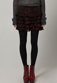 Svart och vinröd volangkjol, lagerdesign, bärs med svarta strumpbyxor och vinröda snörade ankelstövlar. Tröjan har en strukturerad grå finish.