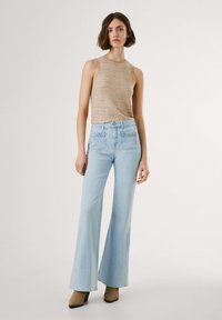 Lichtblauwe uitlopende broek met een hoge taille, voorzien van decoratieve stiksels op de zakken, gecombineerd met een beige gestreept mouwloos topje.