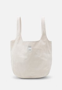 Beżowa torba materiałowa z szerokimi rączkami i małą kwadratową łatą z napisem "SAMSOE SAMSOE" na przednim środku.