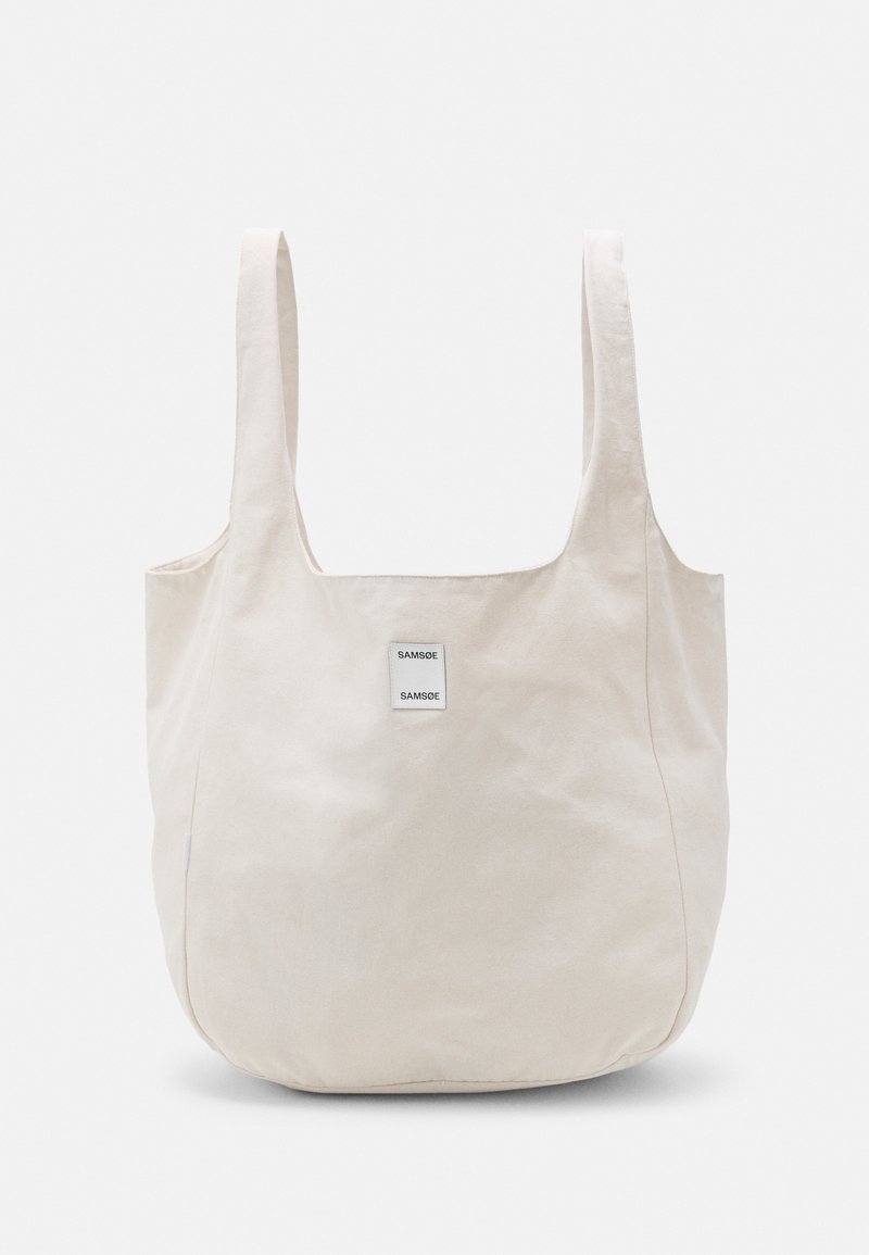 Beżowa torba materiałowa z szerokimi rączkami i małą kwadratową łatą z napisem "SAMSOE SAMSOE" na przednim środku.