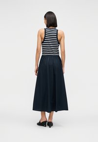 Μακρύ φούστα σε σκο ύρο μπλε με ελαστική μέση, συνδυασμένη με μαύρο-λευκό ριγέ τοπ χωρίς μανίκια, με εφαρμοστό πάνω μέρος και ρευστή φούστα.