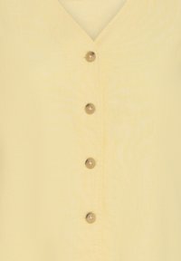 Tissu jaune avec quatre boutons ronds marron alignés verticalement, centrés sur un vêtement à col en V.