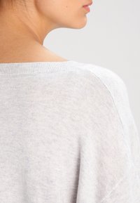 Hellgrauer Strickpullover mit lockerer Passform, weitem Ausschnitt und gerippten Bündchen. Weiche Textur mit subtilen Farbnuancen.