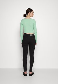Top de mangas longas em verde menta com nervuras, combinado com jeans skinnies pretos de cintura alta. O top é curto, com um decote redondo e silhueta ajustada.