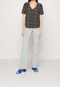 Blusa nera con stampa floreale e maniche a sbuffo corte, abbinata a jeans azzurri a zampa d'elefante e sandali con tacco blocco blu vivace.