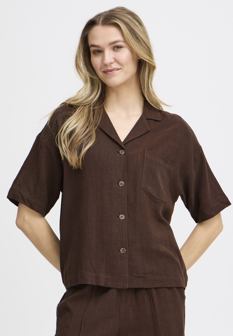 Chemise marron à manches courtes en tissu léger, avec un col, une poche poitrine et des boutons marron sur le devant.