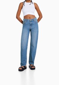 Jeans dritti a vita alta in denim blu chiaro. Abbinati a un top corto bianco e sandali platform neri. Texture liscia, design classico.