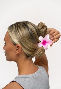 Plastklämma för håret formad som en rosa blomma med en övergång från mörkrosa i mitten till ljusrosa kronblad, som håller ihop en knutfrisyr.