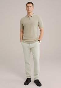 Bežna polo majica s kratkimi rokavi in z zadrgo, teksturirana tkanina, v kombinaciji s svetlo smetanastimi hlačami in črnimi športnimi copati. Preprost dizajn z minimalnimi detajli.