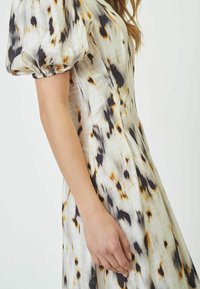 Lightweight dress with puff sleeves, in a cream base featuring black and orange splatter patterns, smooth texture and fitted bodice.