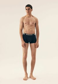 Czarne bokserki męskie z szerokim elastycznym pasem w kontrastowym kolorze z napisem "Henderson", prosty krój, średniej długości.