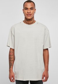 Lys grå oversized t-skjorte med rund hals og rå kanter. Har slitt detaljer på skuldrene og korte ermer.