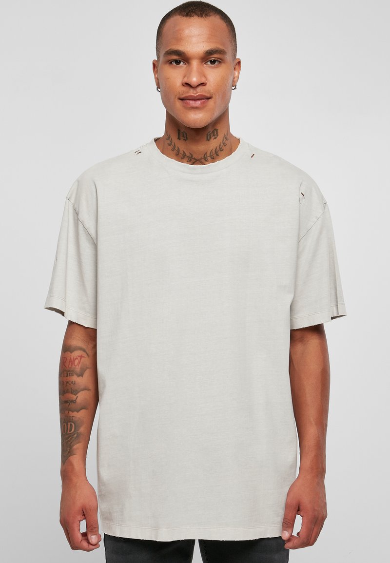 Lys grå oversized t-skjorte med rund hals og rå kanter. Har slitt detaljer på skuldrene og korte ermer.