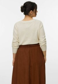 Cremefarvet sweater med opkrøllede ærmer, parret med en brun, mid-længde, let skørt. Outfittet har en bælte i taljen og en glat tekstur.