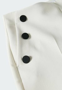 Gros plan sur un tissu de vêtement blanc avec trois grands boutons ronds noirs alignés verticalement sur le bord.