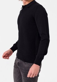 Pull-over noir à manches longues avec un motif en losange, un col polo et des poignets côtelés. Texture lisse avec une coupe ajustée.
