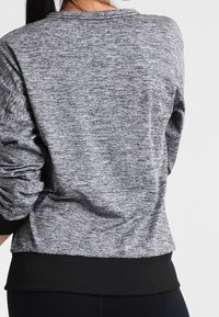 Felpa grigia a maglia con maniche lunghe, caratterizzata da un motivo testurizzato e polsini e orlo a coste neri. La vista posteriore mostra una finitura in tessuto liscia.