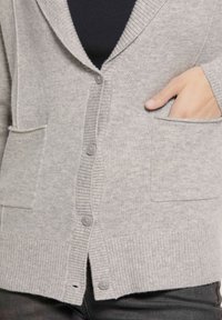 Grijze cardigan met geribbelde accenten, vijf knopen en twee voorzakken. Zachte textuur en open voorkant ontwerp. Minimalistische stijl.